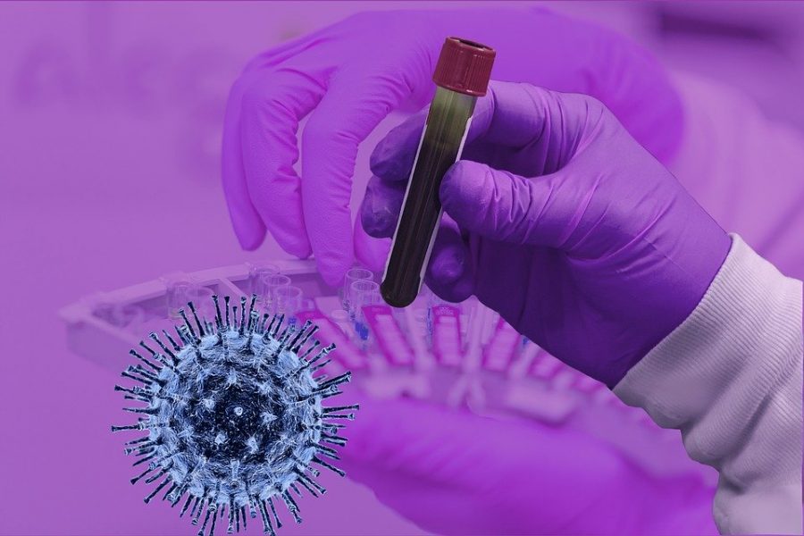 A gloved hand holds up a test tube, next to a picture of the COVID-19 virus