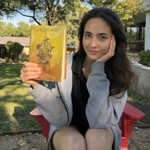 Maya holding a copy of This Woven Kingdom by Tahereh Mafi, which can be found in the library.